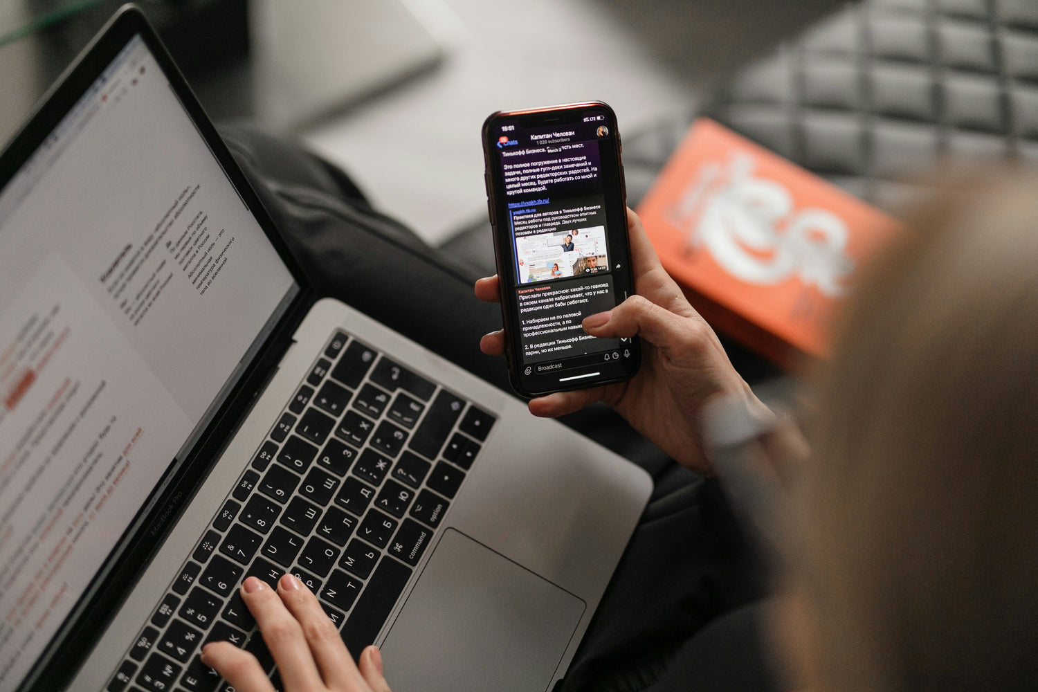 Woman working on a laptop while reading news on her phone